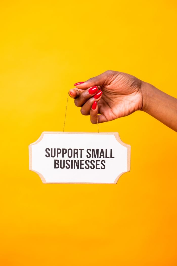 A hand holding a 'Support Small Businesses' sign on a vibrant yellow background.
